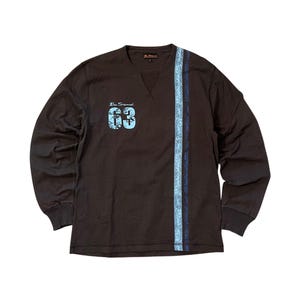 May include: A long-sleeved brown shirt with a blue paisley stripe down the side and the number "63" in blue on the chest. The shirt has a crew neck and ribbed cuffs.