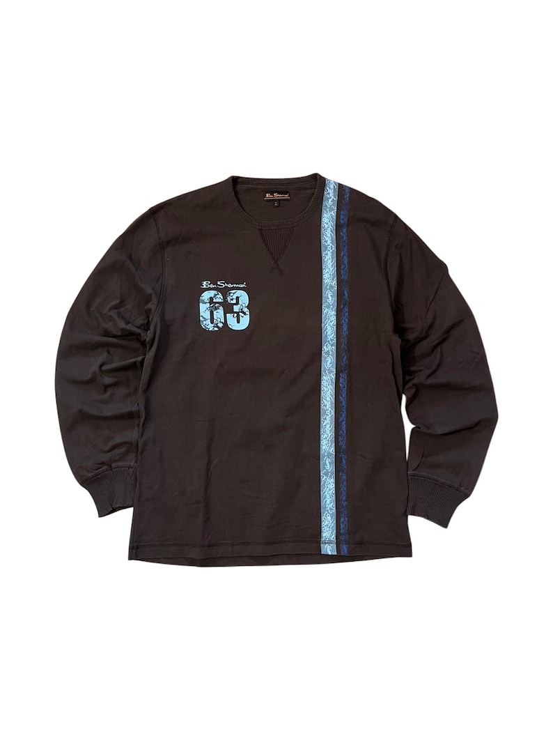 May include: A long-sleeved brown shirt with a blue paisley stripe down the side and the number "63" in blue on the chest. The shirt has a crew neck and ribbed cuffs.