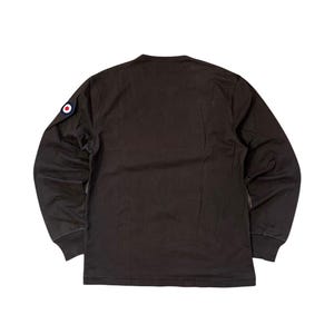 May include: A dark brown long-sleeve shirt with a crew neck. A circular patch with red, white, and blue accents is on the left sleeve. The shirt has ribbed cuffs and a straight hem.