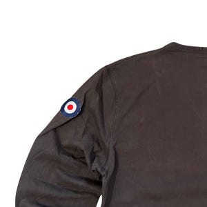 May include: A dark brown long-sleeve shirt with a round patch on the upper left sleeve. The patch is a blue circle with a white border and a red and white center. The shirt is made of a smooth fabric.