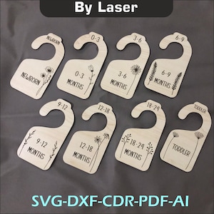 Puede incluir: Conjunto de ocho etiquetas de percha de madera con diseños florales y texto que indica diferentes rangos de edad para la ropa de bebé, incluyendo Recién nacido, 0-3 meses, 3-6 meses, 6-9 meses, 9-12 meses, 12-18 meses, 18-24 meses y Niño pequeño.