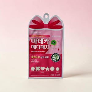 May include: A pink and clear package of Madeca Medi Patch, a product for post-blemish care. The package features a red bow at the top and includes various patch shapes and sizes, including stars, hearts, and circles. The text on the package is in Korean.