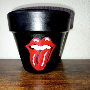 Può includere: Vaso di fiori in terracotta nero con un design di lingua e labbra dipinto in rosso e bianco.