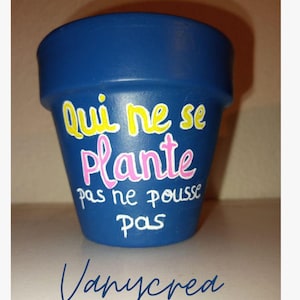 Peut inclure: Un pot de fleurs en terre cuite bleu foncé avec du texte peint à la main en jaune, rose et blanc. La phrase "Qui ne se plante pas ne pousse pas" est inscrite sur le devant. Le mot "Vanycrea" est également imprimé en bleu foncé sous le pot.