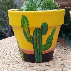 Peut inclure: Un pot en terre cuite jaune avec un motif de cactus peint à la main. Le pot est rempli d'une plante succulente.