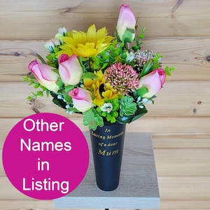 May include: A black vase arrangement with artificial sunflowers, pink roses, and greenery. The vase has gold text reading "In Loving Memory of a dear Mum". A memorial floral tribute.