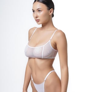 Könnte beinhalten: Weißes Dessous-Set mit einem transparenten BH mit verstellbaren Trägern und einem passenden String. Der BH hat ein zartes, durchsichtiges Design mit kreisförmigen Nippelabdeckungen. Das Set besteht aus leichtem, atmungsaktivem Stoff.