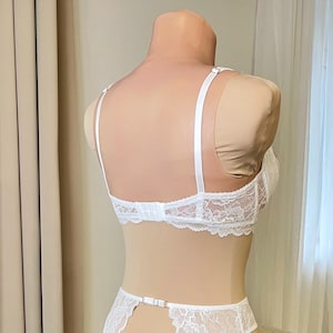 May include: White lace lingerie set with adjustable straps and a hook and eye closure in the back. The set includes a bra and a garter belt.