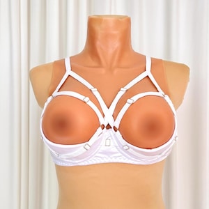 Op de afbeelding: Witte beha met een uniek ontwerp. De beha heeft een satijnen onderbust en een bandjesoverlay. De cups zijn open en de bandjes zijn verbonden met zilverkleurige hardware. De beha wordt op een mannequin getoond.