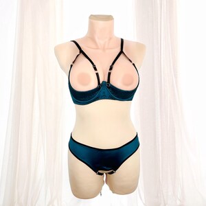 K&ouml;nnte beinhalten: Ein tealfarbenes Dessous-Set auf einer Schaufensterpuppe. Das Set besteht aus einem BH mit offenen Cups und schwarzen Tr&auml;gern sowie einem passenden Slip. Der BH hat ein strukturiertes Design, und der Slip hat einen schwarzen Rand.