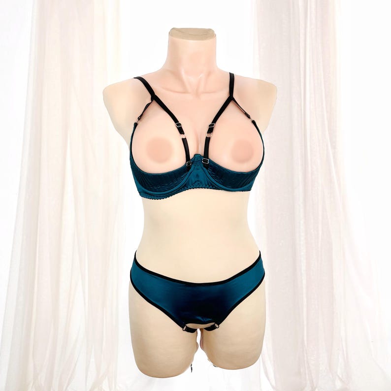 K&ouml;nnte beinhalten: Ein tealfarbenes Dessous-Set auf einer Schaufensterpuppe. Das Set besteht aus einem BH mit offenen Cups und schwarzen Tr&auml;gern sowie einem passenden Slip. Der BH hat ein strukturiertes Design, und der Slip hat einen schwarzen Rand.
