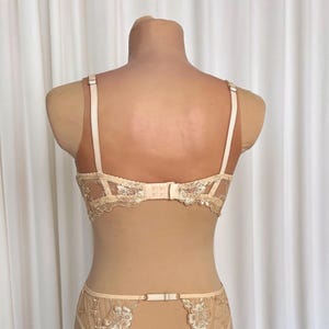 May include: A nude-colored lace bra and panty set with delicate floral embroidery. The bra has adjustable straps and a hook-and-eye closure in the back. The panty has a low-rise cut and a lace trim.