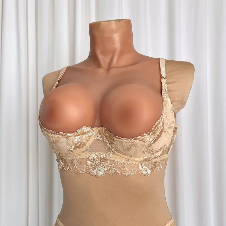 May include: A beige lace bra with gold embroidery. The bra has a plunging neckline and adjustable straps.