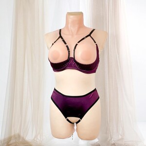 K&ouml;nnte beinhalten: Ein zweiteiliges Dessous-Set in tiefem Lila, pr&auml;sentiert auf einer Schaufensterpuppe. Der BH hat ein einzigartiges offenes Design mit schwarzen Tr&auml;gern und einer samtartigen Textur. Das passende H&ouml;schen hat eine &auml;hnliche Farbe und ein Schl&uuml;ssellochdetail.