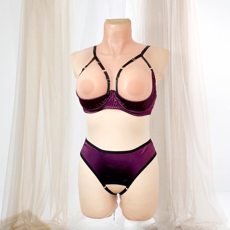 K&ouml;nnte beinhalten: Ein zweiteiliges Dessous-Set in tiefem Lila, pr&auml;sentiert auf einer Schaufensterpuppe. Der BH hat ein einzigartiges offenes Design mit schwarzen Tr&auml;gern und einer samtartigen Textur. Das passende H&ouml;schen hat eine &auml;hnliche Farbe und ein Schl&uuml;ssellochdetail.
