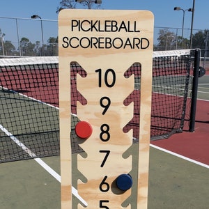 May include: A wooden pickleball scoreboard with numbers 1 through 10. There are red and blue scoring pieces on the scoreboard.