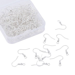 May include: A clear plastic container filled with silver earring hooks. The container is open and there are several earring hooks scattered around it.
