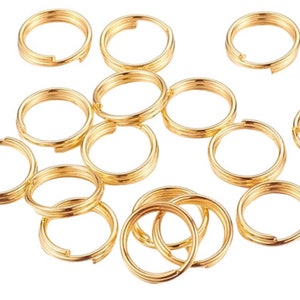 May include: A collection of 13 gold-coloured jump rings, each with a circular shape and a smooth, shiny finish. The rings are arranged in a random pattern on a white background.