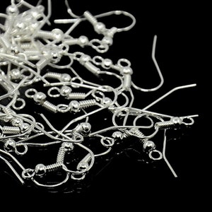 May include: A pile of silver-toned earring hooks with a spring-loaded closure. The hooks are made of metal and have a smooth, shiny finish.