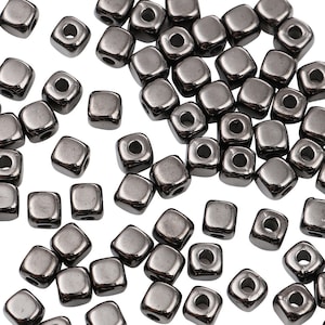 May include: A large quantity of small, black, square beads with a hole in the centre. The beads are made of glass or metal and have a shiny, metallic finish.
