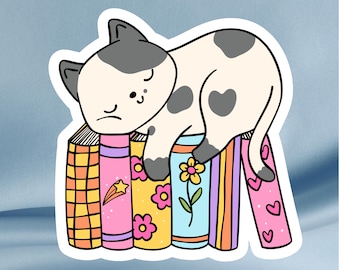 Sticker leesgrage kat – slaperige kat op kleurrijke boeken, lezerscadeau