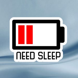 May include: A white sticker with a black border featuring a battery icon with two red bars, indicating low charge. Below the battery graphic, the words "NEED SLEEP" are printed in black.