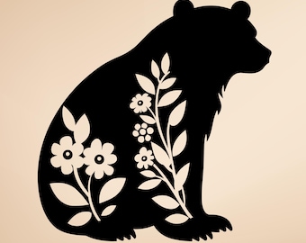 May include: A black silhouette of a sitting bear with white floral and leaf designs. The bear is facing right, with details of the fur and paws. The floral design includes flowers and leaves. The background is a light tan color.