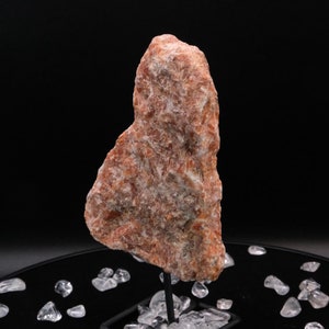 May include: A large, rough, heart-shaped, orange-brown selenite crystal on a black stand with clear quartz crystals surrounding the base.