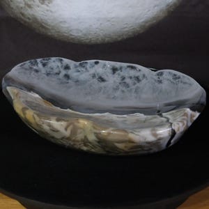 May include: A polished stone bowl featuring a smooth, rounded shape with a natural banded pattern. The surface displays a mix of translucent white, grey, and earthy brown tones with intricate, vein-like textures throughout the mineral structure.