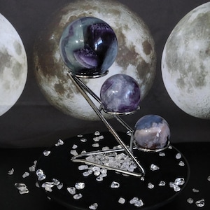 Peut inclure: Un présentoir en métal argenté à trois niveaux supportant trois pierres sphériques polies. La sphère supérieure est violette et verte, celle du milieu est marbrée de violet et blanc, et la sphère inférieure est bleue et blanche.