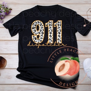 Puede incluir: Camiseta negra con el texto "911 dispatcher" en letras doradas. Los números "911" están rellenos con un estampado de leopardo en blanco y negro. También se ve un gráfico de melocotón y las palabras "Little Peach Designs".