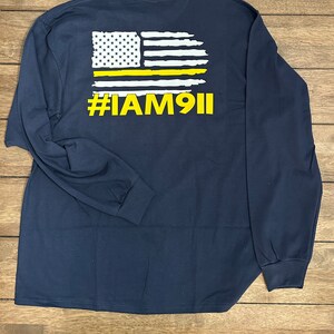 May include: Navy blue long-sleeve t-shirt with a white and yellow American flag graphic and the text "#IAM911" on the back.