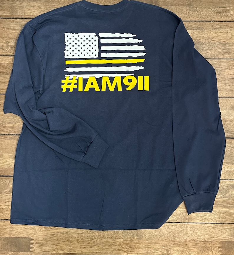 May include: Navy blue long-sleeve t-shirt with a white and yellow American flag graphic and the text "#IAM911" on the back.
