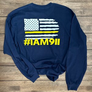 May include: Navy blue long-sleeve t-shirt with a white and yellow American flag graphic and the text "#IAM911" printed on the back.