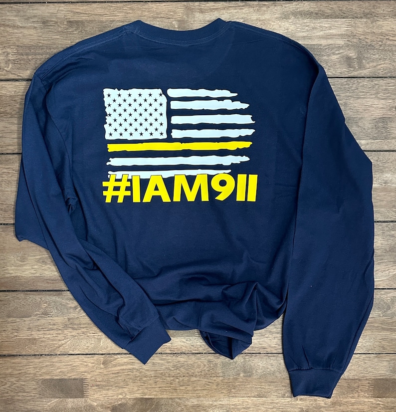 May include: Navy blue long-sleeve t-shirt with a white and yellow American flag graphic and the text "#IAM911" printed on the back.