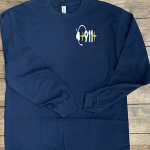May include: Navy blue long-sleeve t-shirt with a white graphic of a headset and the text "911" with a yellow heartbeat graphic.