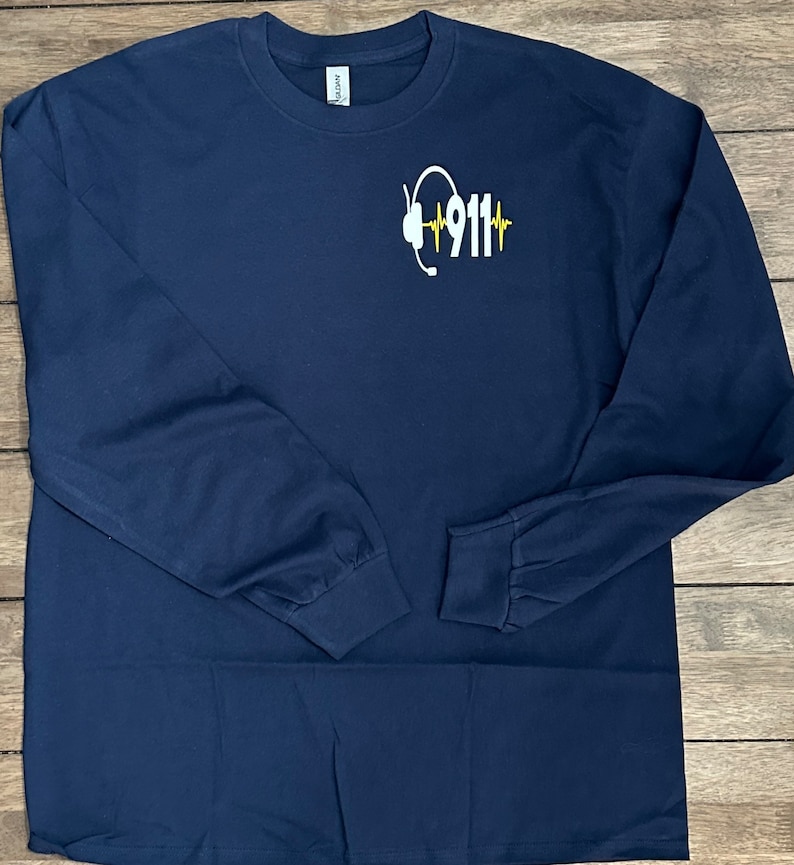 May include: Navy blue long-sleeve t-shirt with a white graphic of a headset and the text "911" with a yellow heartbeat graphic.