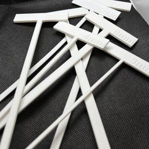 May include: A collection of white plastic T-shaped tools, each labeled with a measurement in millimeters. The tools are scattered on a dark textured surface. The measurements visible are 3mm, 4mm, 5mm, 6mm, 7mm, and 8mm.