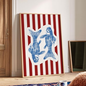 Può includere: Una stampa incorniciata con uno sfondo a strisce rosso e bianco e due pesci blu al centro. I pesci si guardano e sono in un design stilizzato.