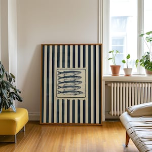 May include: A framed art print featuring a rectangular image of five fish. The fish are in a rectangular frame, set against a background of navy blue and cream vertical stripes. The frame is a light brown color.
