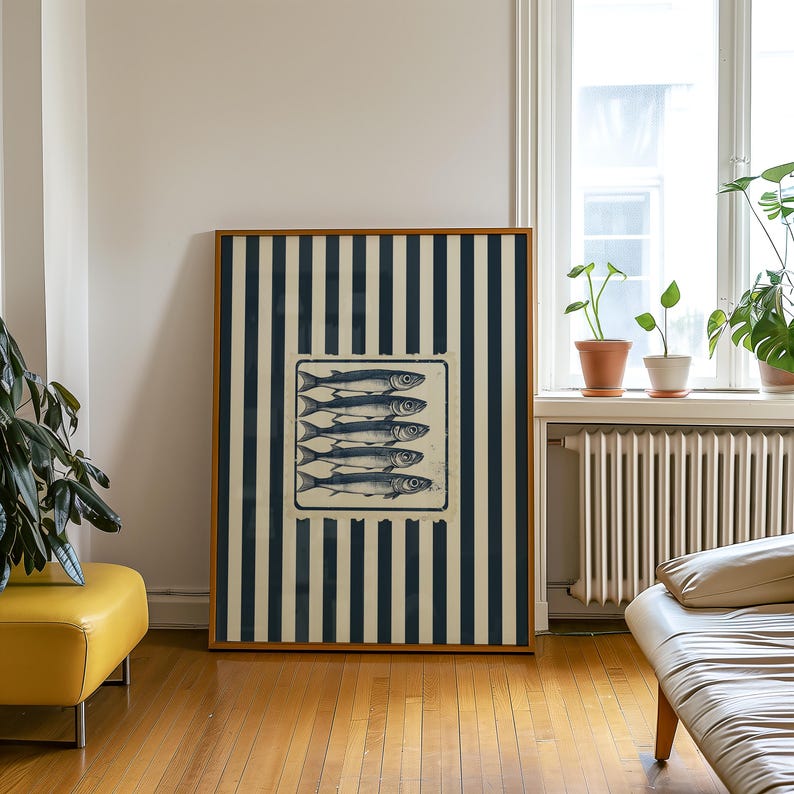 May include: A framed art print featuring a rectangular image of five fish. The fish are in a rectangular frame, set against a background of navy blue and cream vertical stripes. The frame is a light brown color.