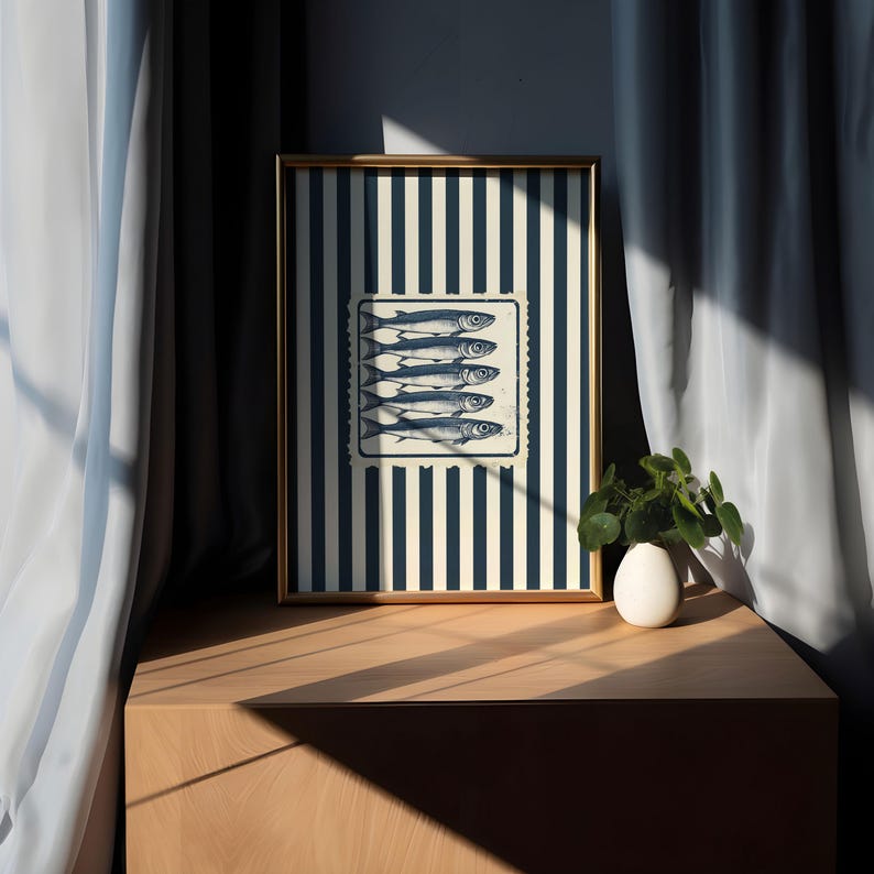 May include: A framed art print featuring a nautical theme. The artwork displays a rectangular image of six fish, set against a striped background of navy blue and cream. The frame is gold-colored, and the print is displayed on a wooden surface.