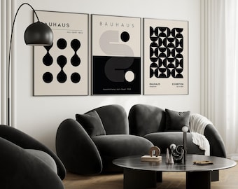May include: Three black and white geometric art prints with the text "Bauhaus Exhibition" on the rightmost print. The prints are hanging on a white wall above a black sofa.