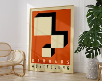 May include: A framed Bauhaus art print with an abstract geometric design in black, cream, and orange. The words "BAUHAUS AUSTELLUNG" are printed in white at the bottom. The print is displayed in a light-coloured wooden frame, leaning against a white wall.