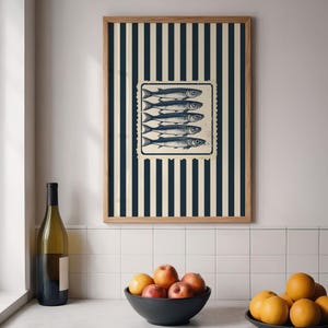 May include: A framed print featuring a vintage-style illustration of five fish on a striped background. The artwork is in a wooden frame and is displayed above a countertop with a bowl of fruit and a wine bottle.