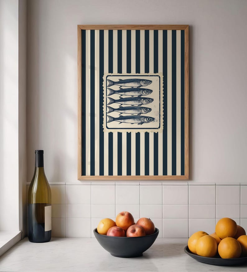 May include: A framed print featuring a vintage-style illustration of five fish on a striped background. The artwork is in a wooden frame and is displayed above a countertop with a bowl of fruit and a wine bottle.