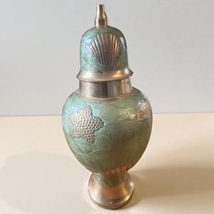 Peut inclure: Un vase décoratif de style vintage, avec un schéma de couleurs vert et or. Le vase présente un motif de coquillage sur le couvercle et un motif en forme d'étoile sur le corps. La base et les accents sont de couleur or.