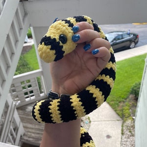 May include: A yellow and black striped crocheted snake toy. The snake is curled up and has large, black eyes.