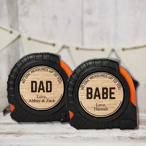 May include: Two black and orange tape measures with wooden inserts. The first tape measure reads "No one measures up to you Dad Love, Abbey & Zack". The second tape measure reads "No one measures up to you Babe Love, Hannah".