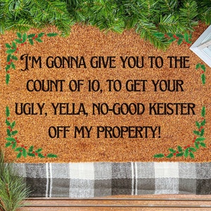 May include: A brown coir doormat with a Christmas-themed design. The text on the mat reads "I'M GONNA GIVE YOU TO THE COUNT OF 10, TO GET YOUR UGLY, YELLA, NO-GOOD KEISTER OFF MY PROPERTY!"